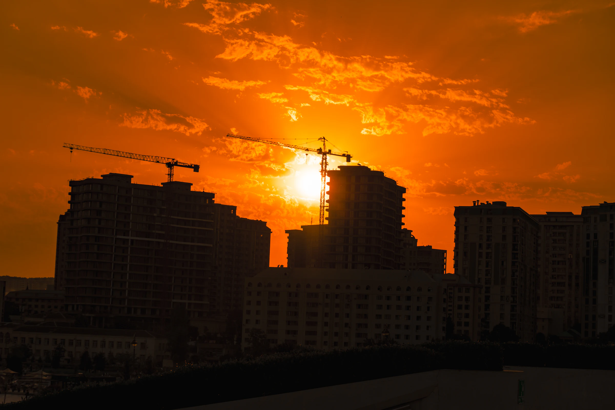 Construction cranes silhouetted over a city at sunset