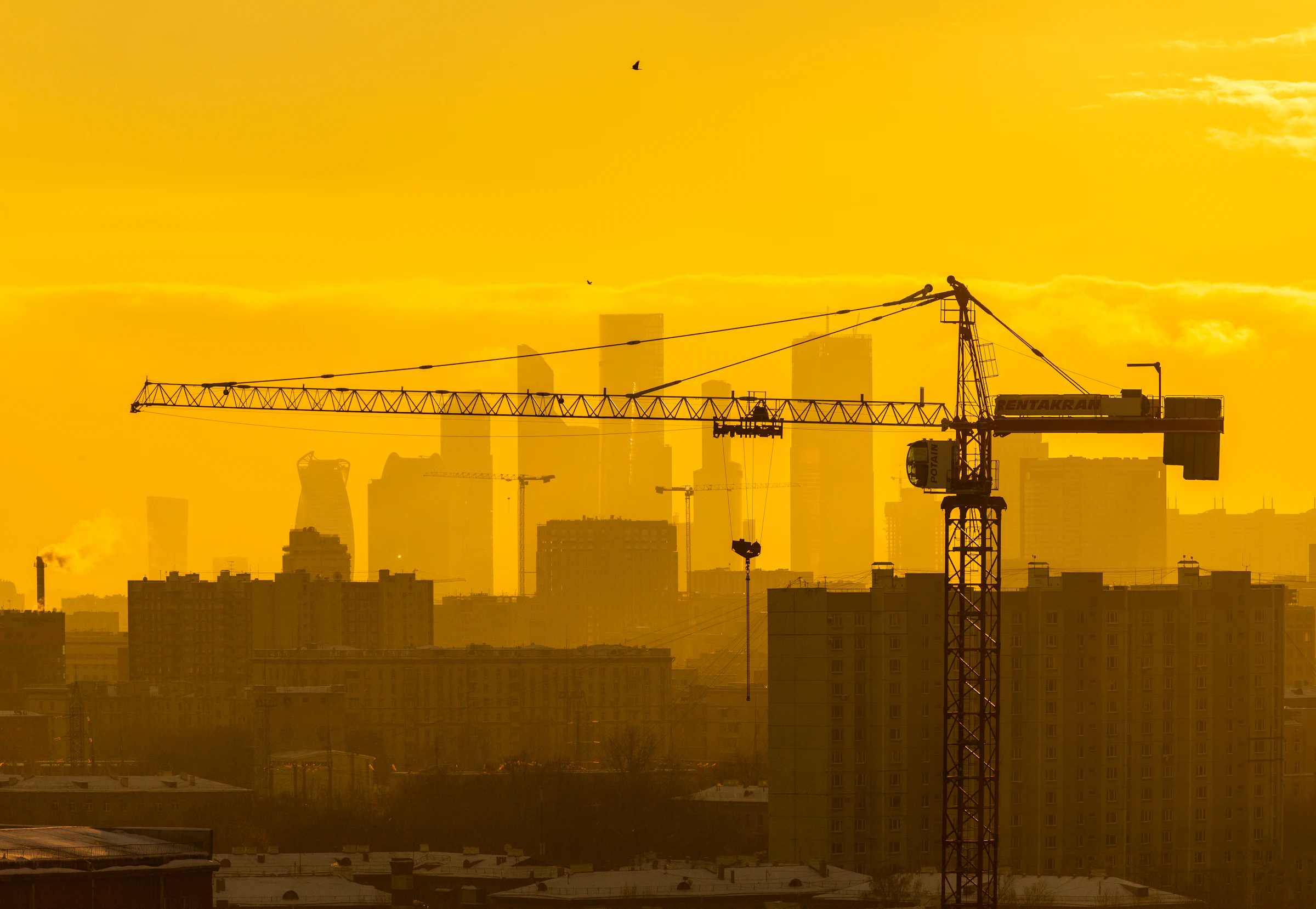Tower crane silhouetted against a city skyline at golden hour